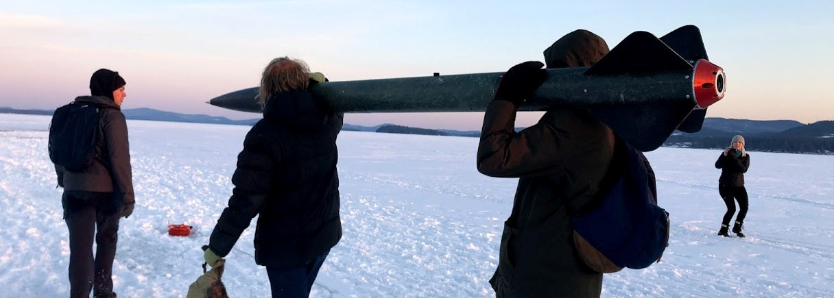 People carrying a rocket across a frozen lake